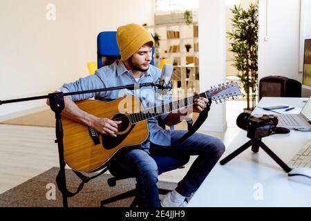 Musicista che suona la chitarra mentre riproduce in streaming dal vivo attraverso la telecamera durante la registrazione studio Foto Stock