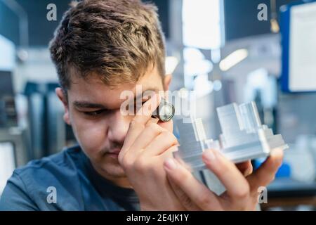 Tecnico con un piccolo microscopio che esamina il modello mentre si è in piedi all'industria Foto Stock