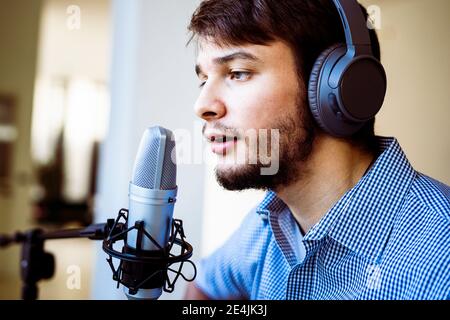 Cantante con cuffie utilizzando il microfono mentre canta in studio di registrazione Foto Stock