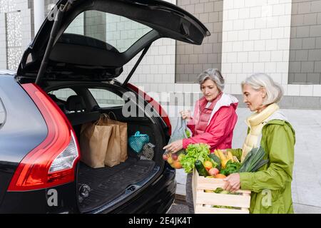 Amici di sesso femminile che caricano generi alimentari nel bagagliaio dell'auto Foto Stock