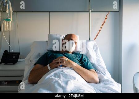 Paziente che indossa una maschera protettiva per il viso utilizzando il telefono cellulare mentre si trova a letto in ospedale Foto Stock