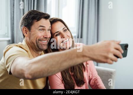 Felice coppia matura che parla selfie attraverso il telefono cellulare a casa Foto Stock