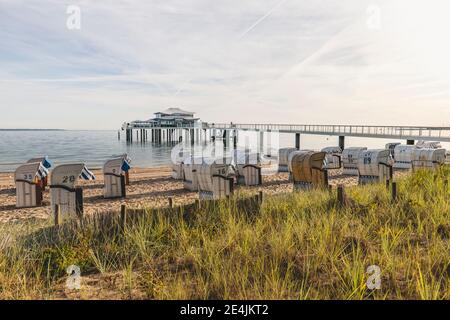 Germania, Schleswig-Holstein, Timmendorfer Strand, sdraio con cappuccio sulla spiaggia sabbiosa costiera con teawhouse alla fine del molo in background Foto Stock