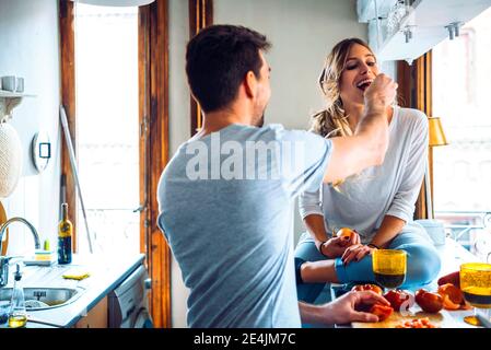 Giovane uomo che prepara il cibo e che alimenta la ragazza in cucina a. casa Foto Stock