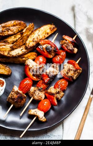 Gyros spiedini di pollo speziati con pomodori, peperoni, zeppe di patate sul tavolo Foto Stock