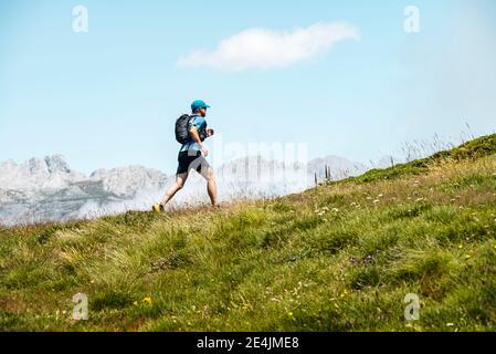 Percorso sportivo maturo che corre in montagna sul prato contro il cielo blu Foto Stock