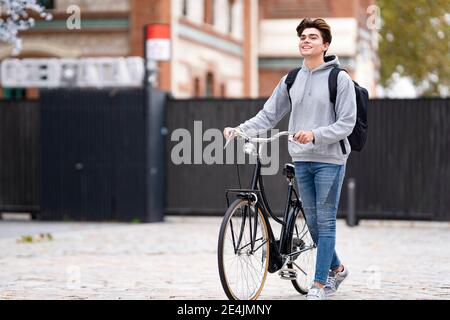 Sorridente giovane alla moda con zaino in bicicletta sul sentiero in città Foto Stock