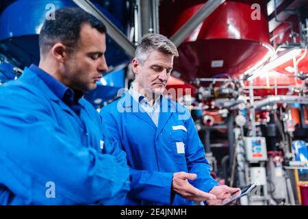 I tecnici maturi discutono di tablet digitale mentre lavorano in fabbrica Foto Stock