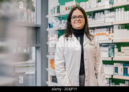 Un farmacista sicuro indossa un camice da laboratorio mentre si trova in una farmacia Foto Stock