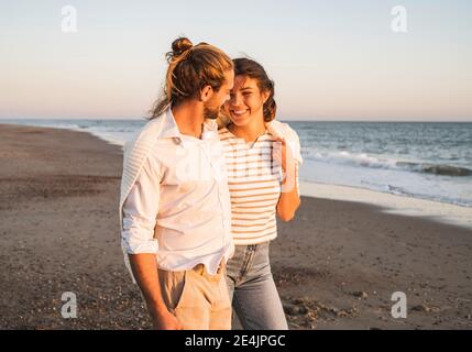 Giovane donna sorridente che cammina con il ragazzo in spiaggia durante il tramonto Foto Stock