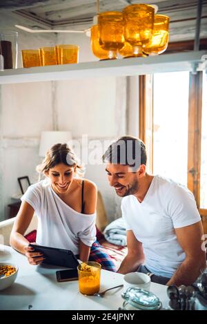 Felice giovane coppia che guarda il tablet mentre si ha la colazione a casa Foto Stock