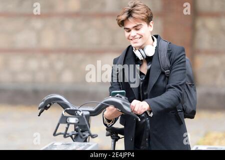 Sorridente giovane che usa lo smartphone per sbloccare la condivisione elettrica bicicletta in città Foto Stock