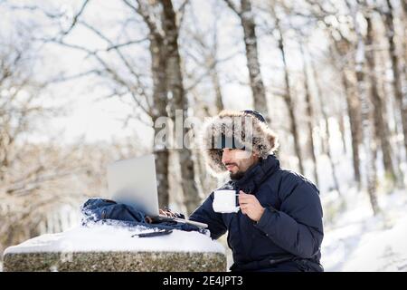 Uomo d'affari che ha il caffè mentre lavora su un computer portatile nella neve Foto Stock