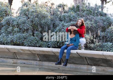 Giovane donna che copre gli occhi della ragazza nel parco pubblico Foto Stock
