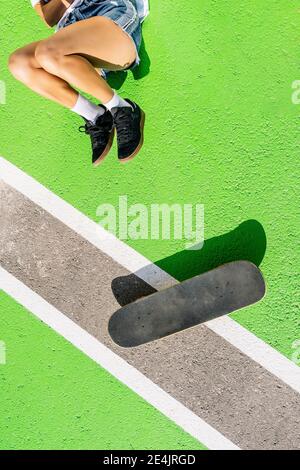 Donna adulta sdraiata con skateboard su superficie verde Foto Stock