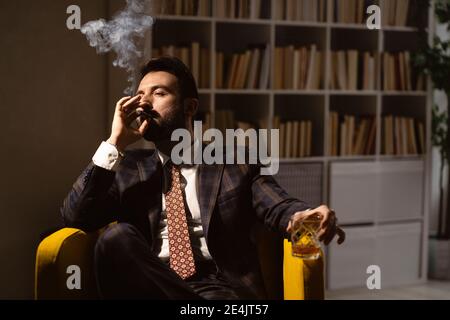 Ritratto di uomo bearded godendo di sigaro e bicchiere di whisky Foto Stock