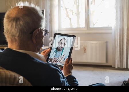 Uomo anziano che prende consiglio dal medico di sesso maschile in videochiamata tramite tablet digitale a casa Foto Stock