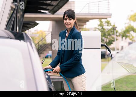 Donna sorridente imprenditore che collega il caricabatterie in auto elettrica Foto Stock