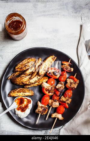 Gyros spiedini di pollo con pomodori, peperoni, spicchi di patate in piatto da tzatziki sul tavolo Foto Stock