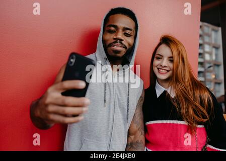 Sorridendo amici multietnici che prendono selfie da sfondo rosso Foto Stock