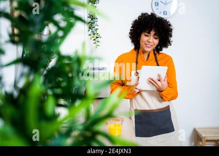 Giovane donna che indossa un grembiule utilizzando un tablet digitale mentre si sta in piedi casa Foto Stock