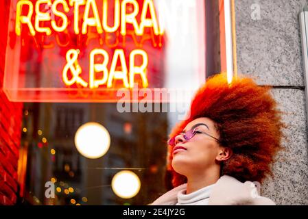 Donna elegante con capelli afro che indossa occhiali da sole contro il ristorante Foto Stock