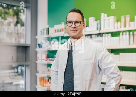 Un farmacista sorridente che indossa un camice da laboratorio mentre si trova in una farmacia Foto Stock