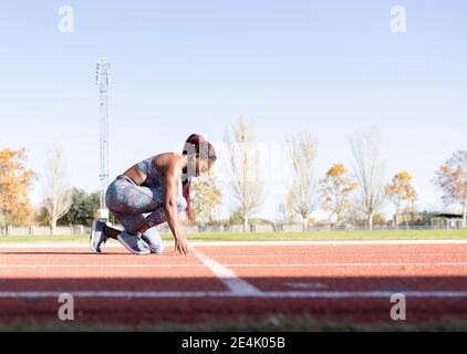 Sportivo femminile in posizione di partenza su pista sportiva durante il sole giorno Foto Stock