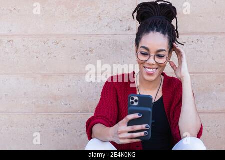 Sorridente bella giovane donna con Dreadlock che prende selfie contro muro Foto Stock