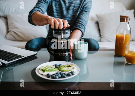 Uomo che usa la macchina per il caffè mentre fa colazione sul tavolo a casa Foto Stock