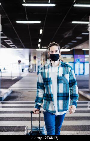 Giovane uomo che indossa la maschera che cammina con i bagagli sul sottopassaggio strada Foto Stock