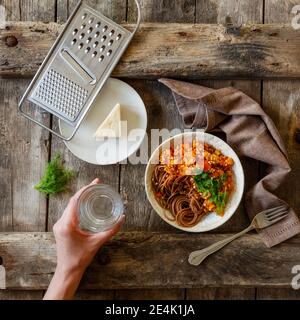 Ciotola di spaghetti vegetariani bolognesi e mano di donna che tiene bicchiere d'acqua Foto Stock