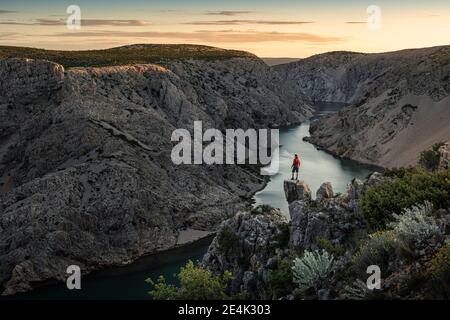 Uomo in piedi su rocce e guardando il fiume in canyon al tramonto Foto Stock