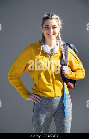 Sportswoman sicuro con borsa per il trasporto alla cintura mentre si trova contro la parete grigia Foto Stock