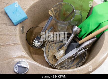 pile di piatti sporchi nel lavandino, guanti in lattice verde e spugna con detergente liquido Foto Stock