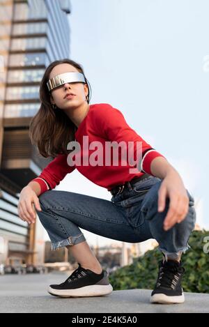 Donna elegante con occhiali da sole accovacciati sul sentiero in città Foto Stock