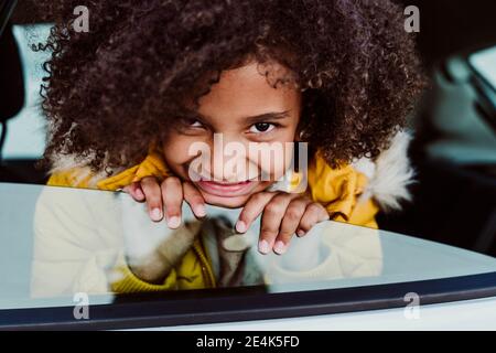 Primo piano di sorridente ragazza con capelli ricci che picchiano in auto finestra Foto Stock