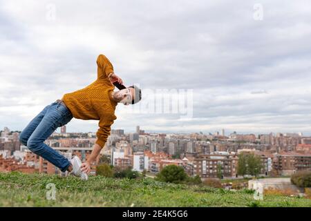 Giovane uomo che parla sul telefono cellulare mentre fa attività acrobatica contro il paesaggio urbano Foto Stock