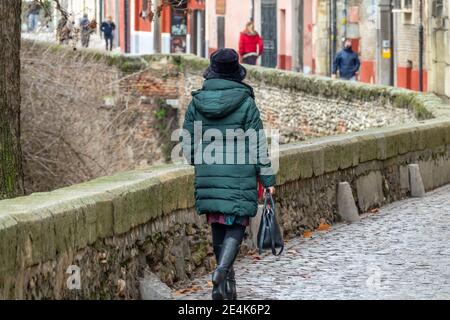 Donna con cappello, stivali alti e borsa visto da dietro a piedi lungo la Carrera del Darro a Granada (Spagna) in una fredda giornata invernale Foto Stock