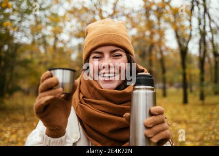 Donna felice in cappello a maglia con bottiglia in acciaio inox a. parco autunnale Foto Stock