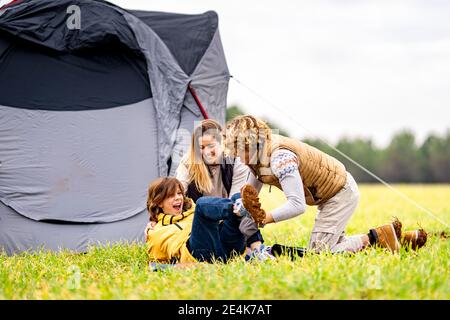 Tre fratelli che giocano sull'erba davanti alla tenda a pitched Foto Stock