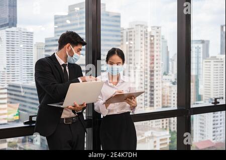 Multi-etnico collega di affari che indossa la maschera di faccia discutere e consultare in un nuovo ufficio normale nel distretto di affari. Mentre pandemia di Coronavirus, Foto Stock