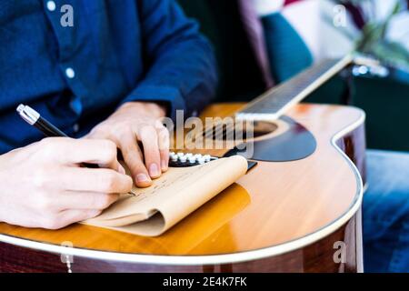 Scrittore di canzone che scrive musica sul blocco note mentre si è seduti con chitarra in studio Foto Stock