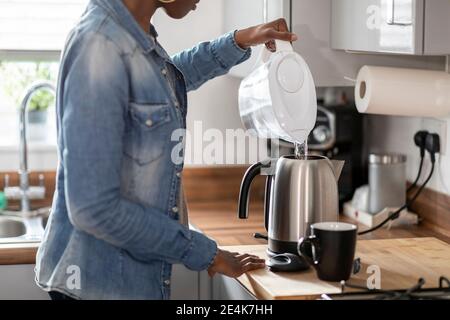 Donna che versa acqua nel bollitore in cucina Foto Stock