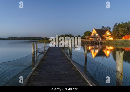 Germania, Schleswig-Holstein, Hemmelsdorf, molo vuoto sulla riva di Hemmelsdorfer vedere il lago all'alba con la casa in background Foto Stock
