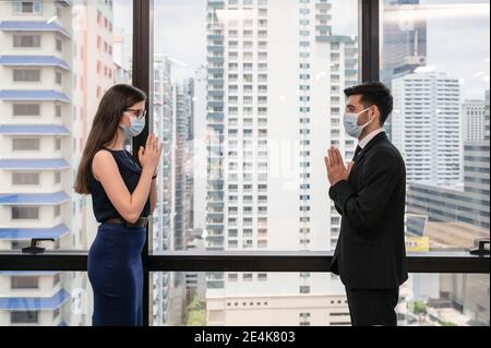 Giovane collega caucasico di affari che indossa la maschera di faccia con lo stile thailandese saluto per il concetto di distanting sociale nel nuovo ufficio normale a. in centro Foto Stock