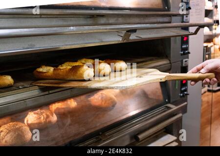 Chef maschile che taking out pane appena sfornato con buccia di pizza dal forno alla panetteria Foto Stock