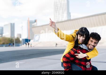 Donna sorridente che punta mentre piggybacking sull'uomo all'aperto Foto Stock