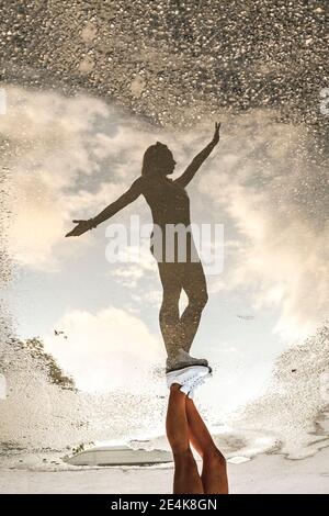 Riflessione di donna con le braccia allungate sulla puddle durante la vacanza Foto Stock