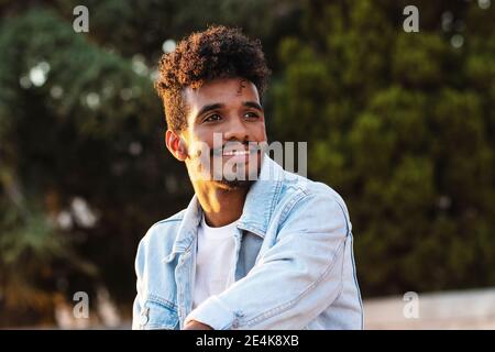 Primo piano di un giovane sorridente e premuroso seduto contro gli alberi parcheggio Foto Stock